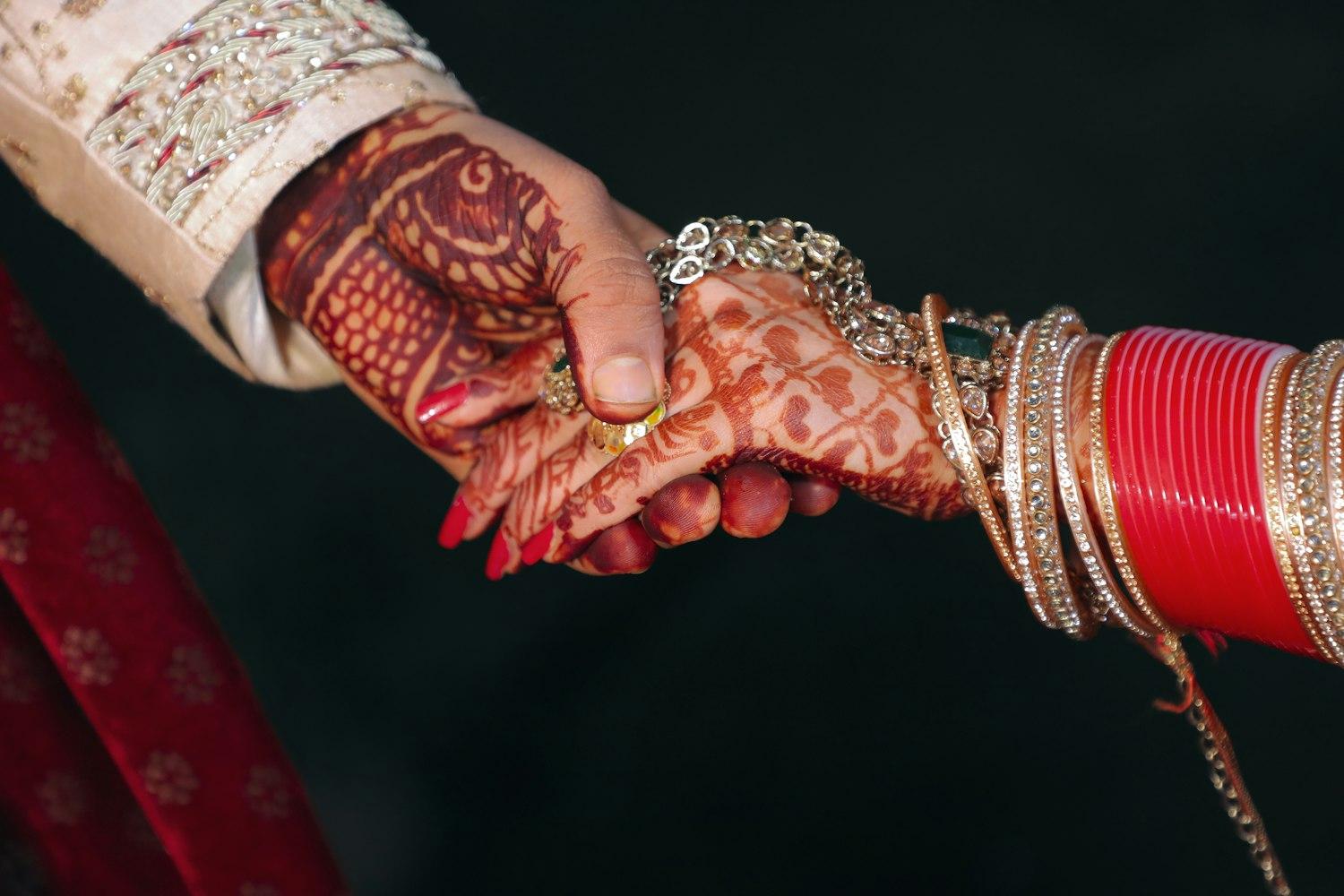 A couple's hands clasped, the bride's mehendi and chooda against the groom's sherwani